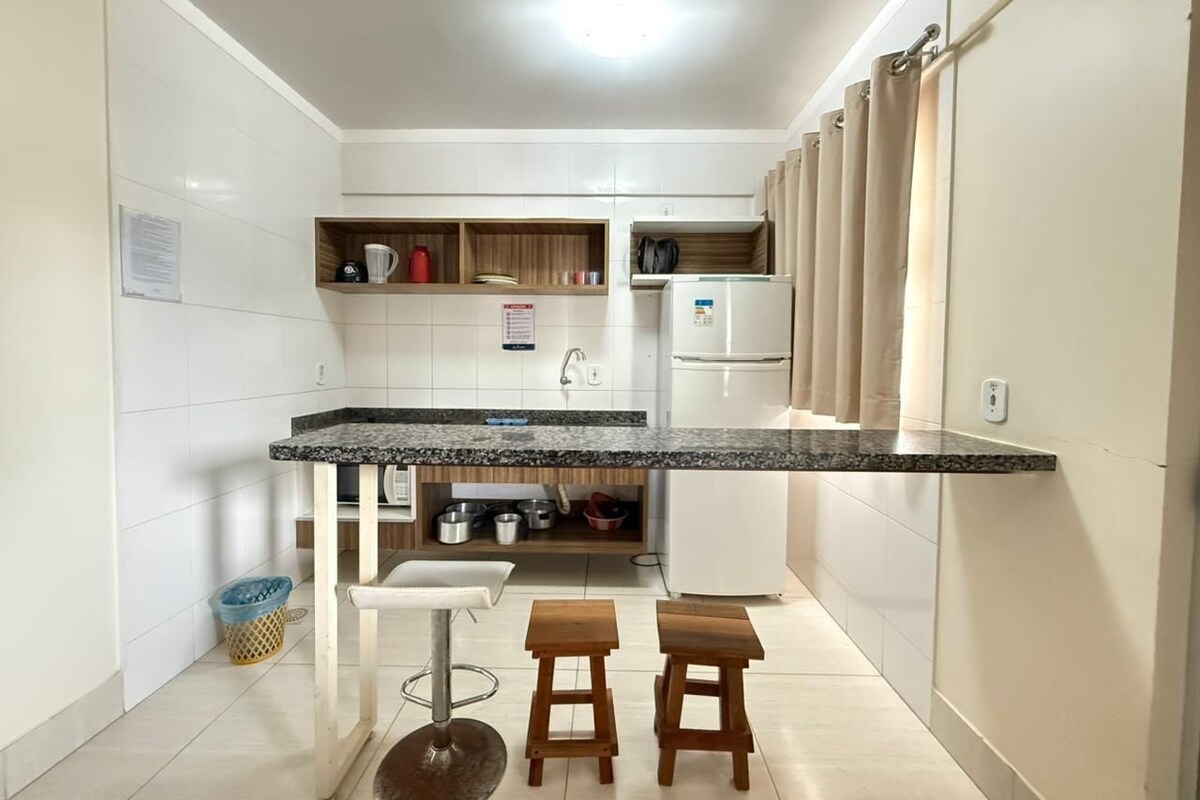 Cocina compacta con encimera de granito, armarios blancos, horno integrado y un pequeño rincón de comedor con taburetes.