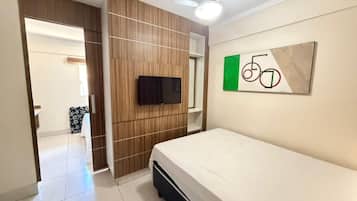 Quarto com cama, televisão, ventoinha no teto e obra de arte na parede.