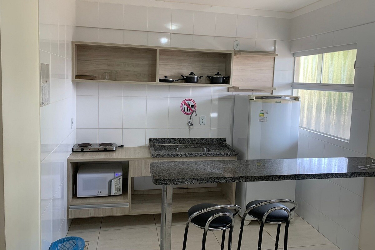 Una cocina compacta con baldosas blancas, microondas integrado, estufa y refrigerador.