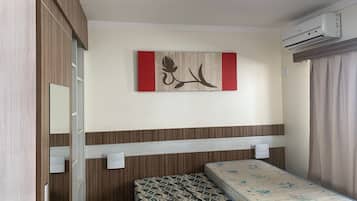 A bedroom with a bed, a wall-mounted air conditioner, a wooden wardrobe, a mirror, and a decorative piece.