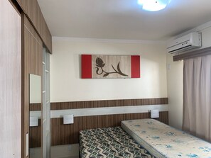 Un dormitorio con cama, aire acondicionado de pared, armario de madera, espejo y un adorno decorativo.