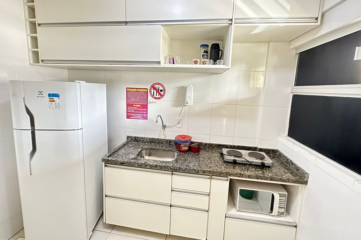 Cocina compacta con refrigerador, microondas, fregadero y una pequeña encimera con hervidor y cafetera.