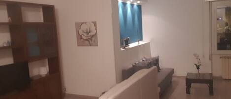 A living room with a white sofa, a wooden cabinet, a small table with a plant, and a window with curtains.