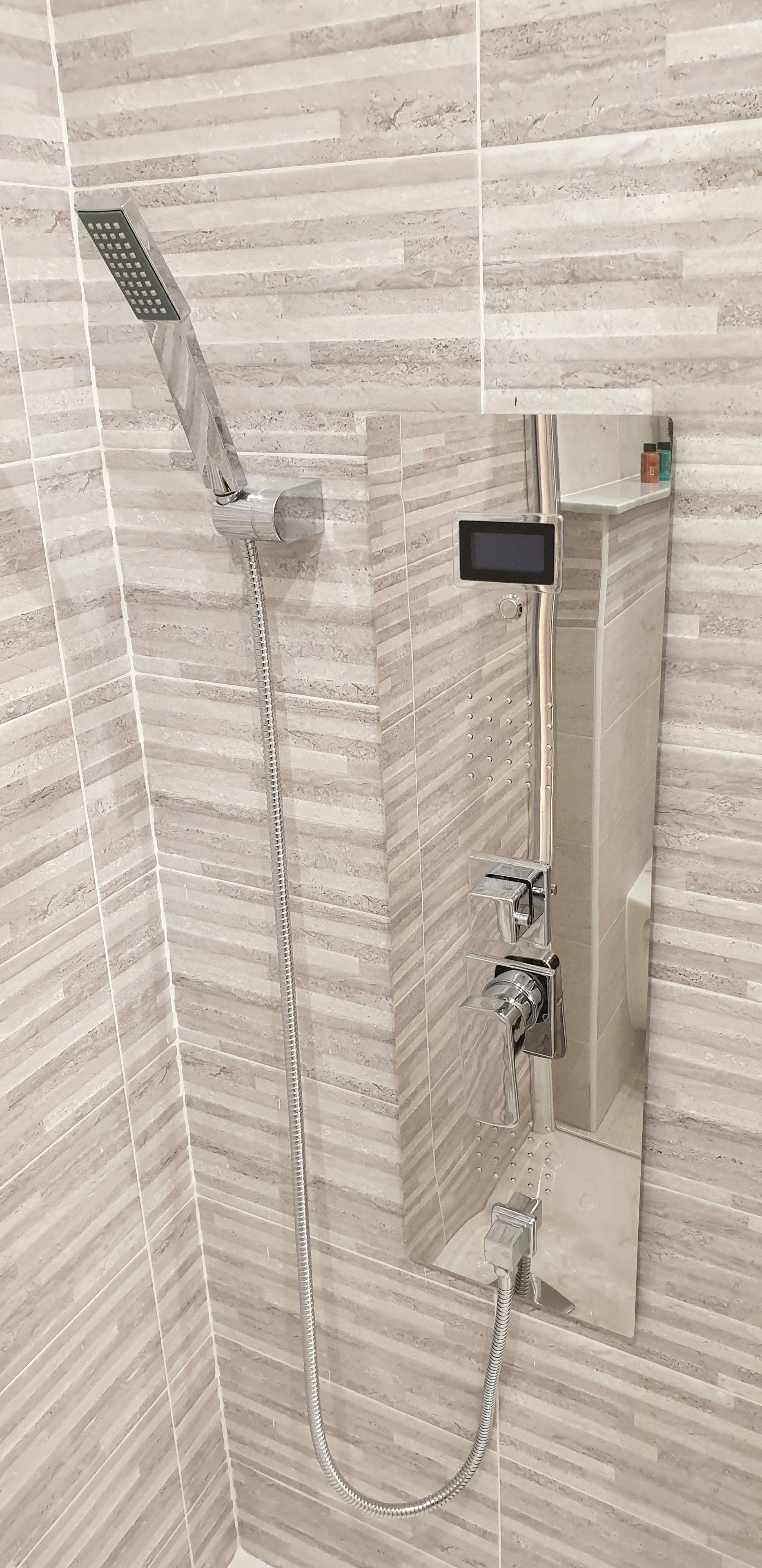 Un baño moderno con ducha, cabezal de ducha manual y un panel de control.