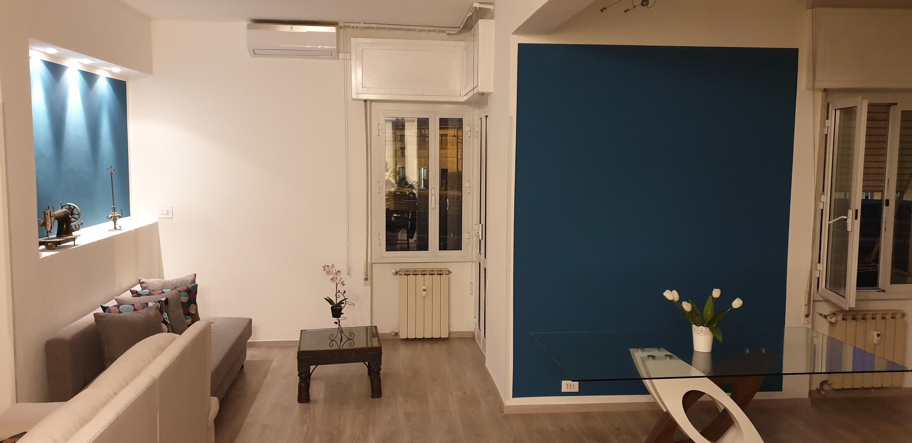 Un soggiorno moderno con un divano, un tavolino in vetro e una parete blu a contrasto.