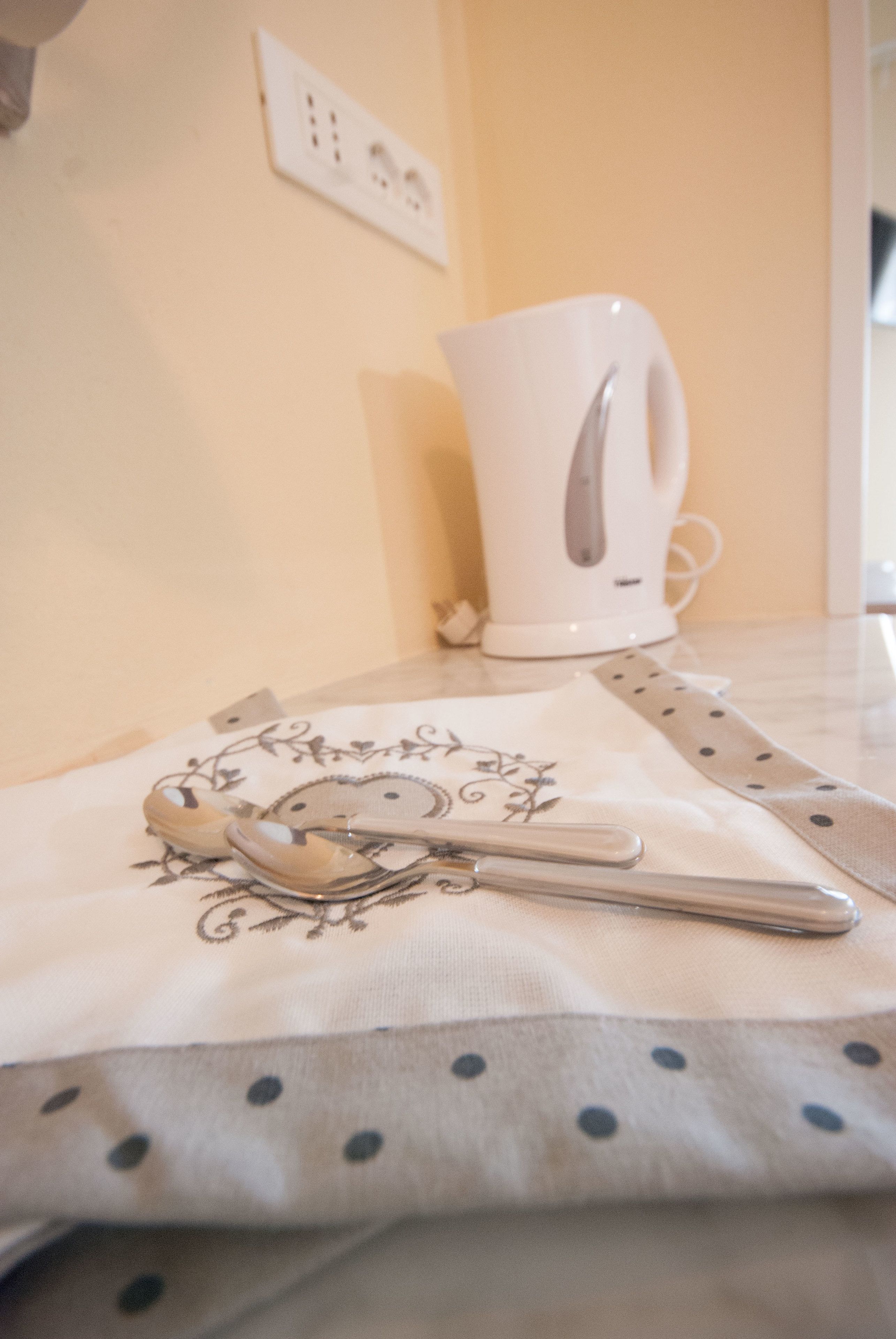 A kitchen counter with a white kettle, a spoon, and a cloth with a floral pattern.