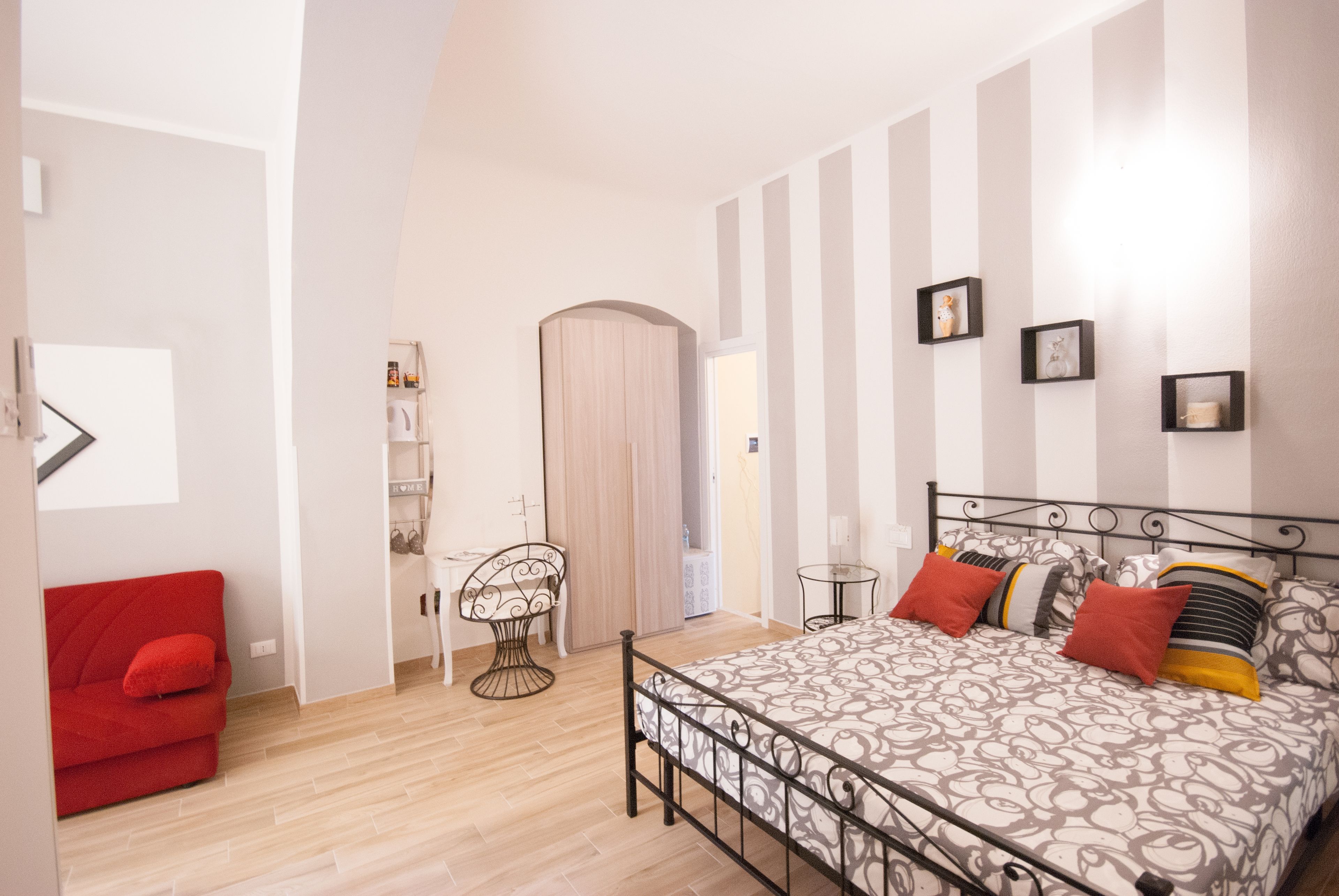 A bedroom with a bed, a red chair, a small table, and a wardrobe.