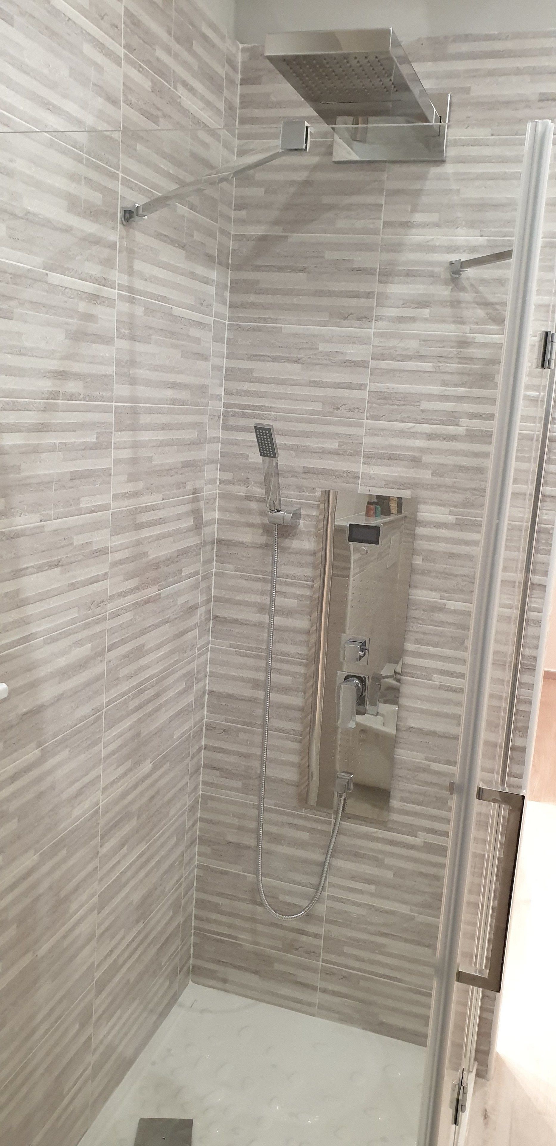 A shower with a glass door, a handheld showerhead, and a wall-mounted control panel.