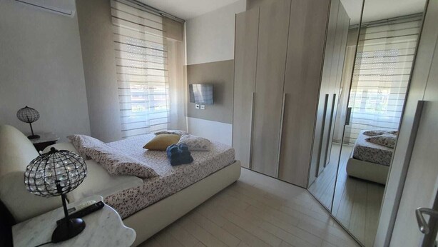 A bedroom with a bed, a bedside table with a lamp, a TV, and a large mirror.