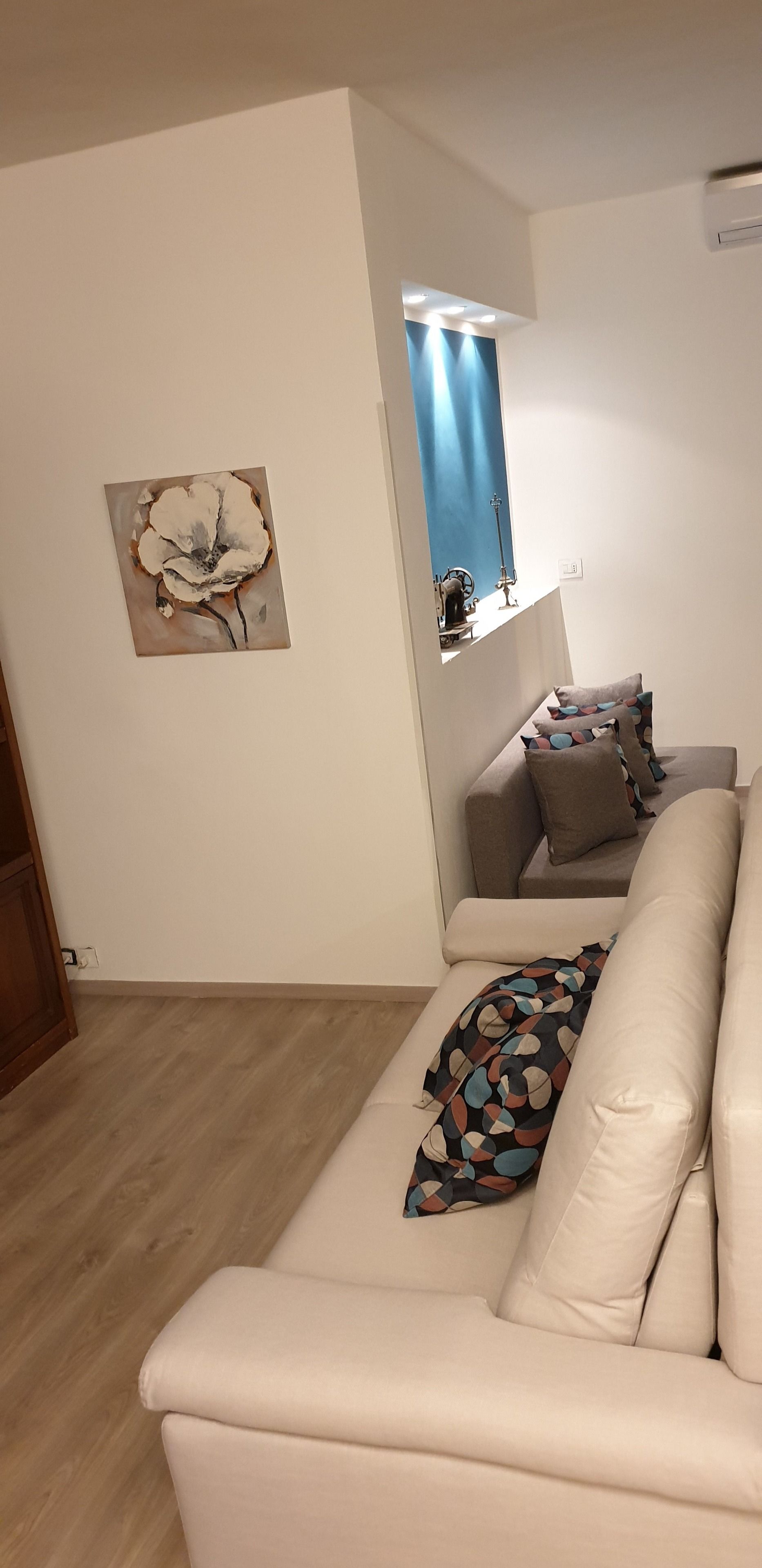 Un salon avec un canapé beige, un plaid coloré et un tableau accroché au mur.
