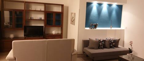 A living room with a sofa, a television, a cabinet, and a window with a sewing machine.