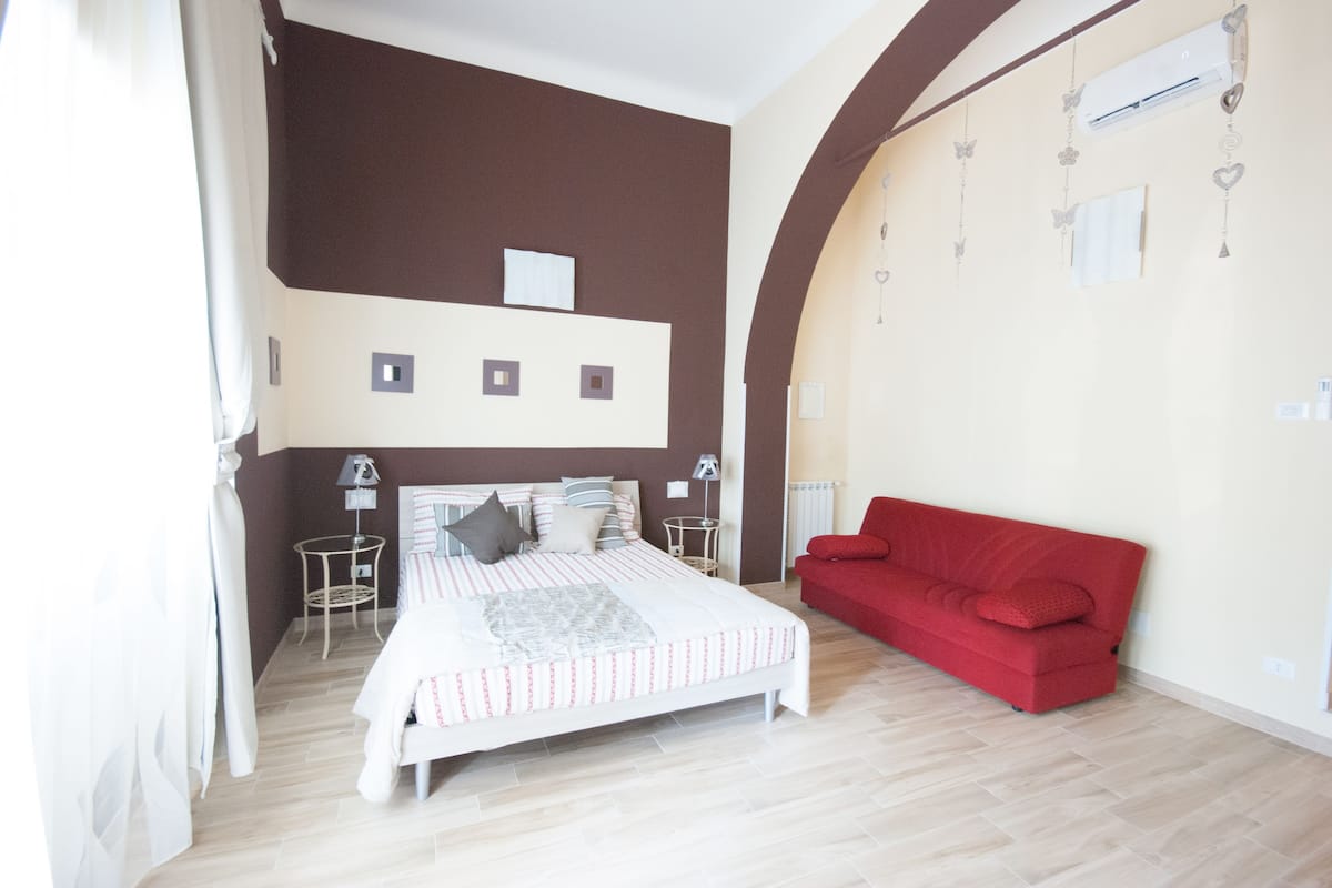 Ein Schlafzimmer mit einem Bett, einem roten Sofa, einem kleinen Tisch und einer Wand-Klimaanlage.