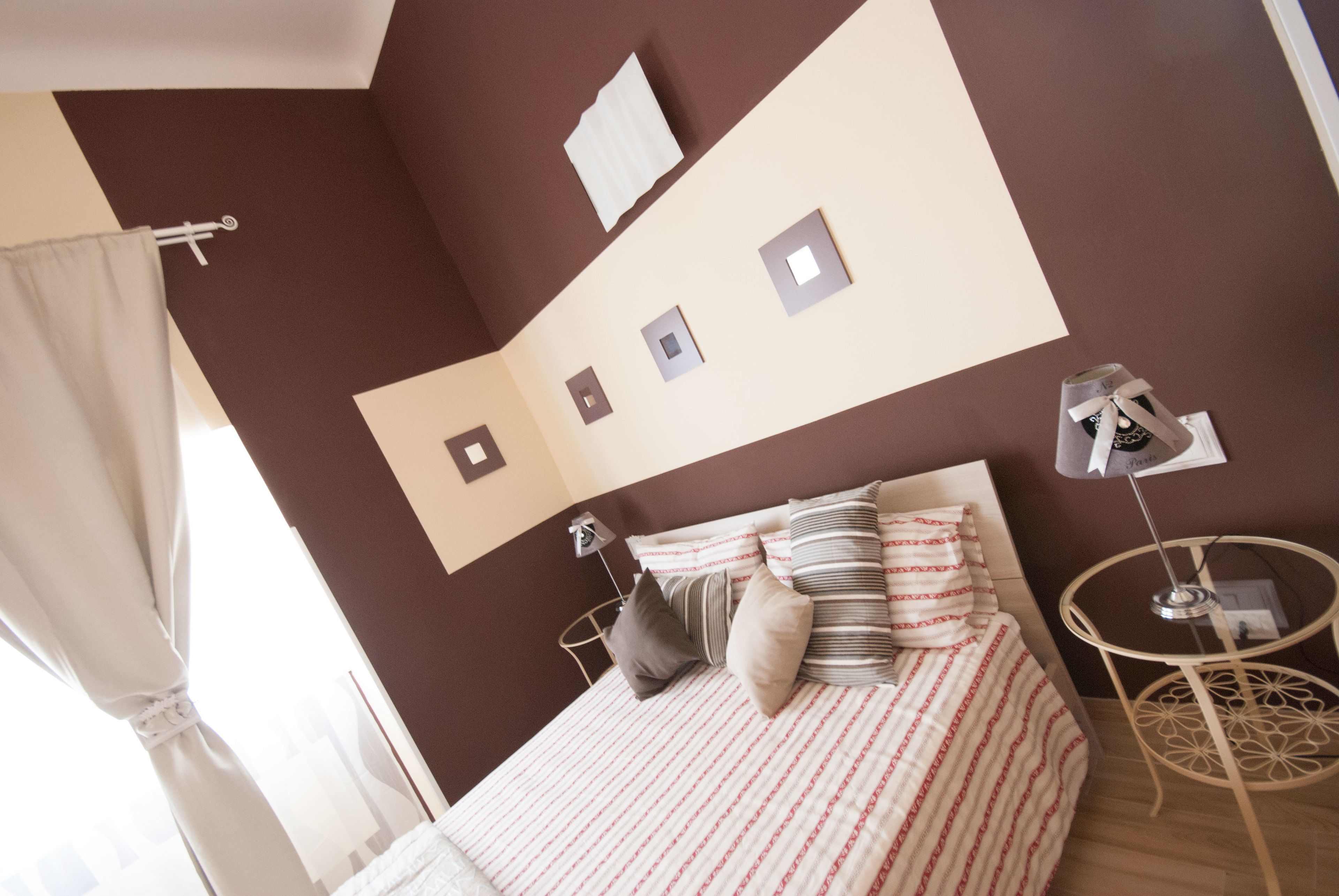 A bedroom with a bed, pillows, a bedside table, a lamp, and a wall-mounted shelf.