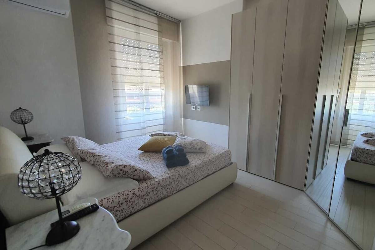 Ein Schlafzimmer mit einem Bett, einer Nachttischlampe, einem Fernseher und einem großen Spiegel.