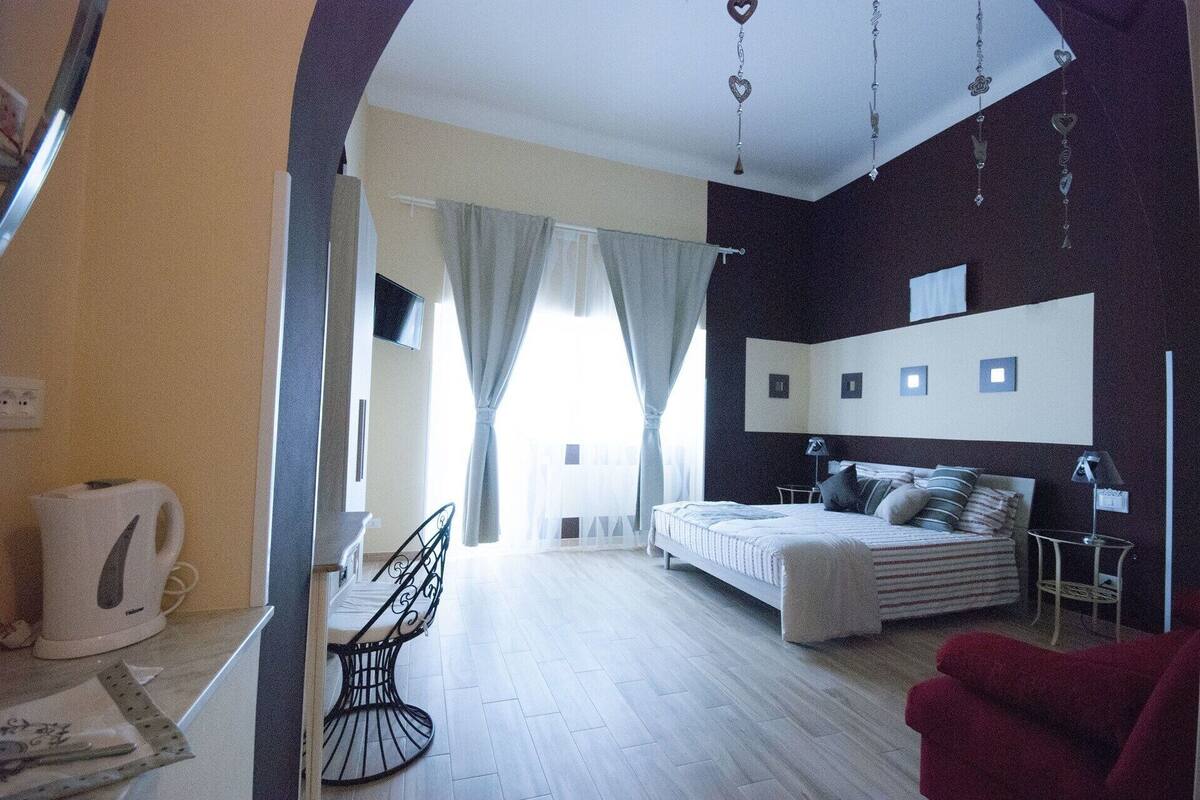 Ein Schlafzimmer mit einem Bett, Nachttischen, einem Fernseher und einem Fenster mit Vorhängen.