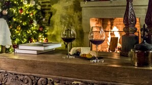 A wooden table with two wine glasses, a book, and a plate of snacks. A Christmas tree and a fireplace are in the background. - Ida Blue, Adatepe - Adults Only (Ayvacik)