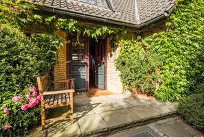 Een knus huis met een bakstenen gevel, een houten bank en een deur met groene luiken.