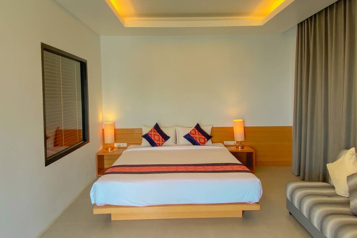 Een hotelkamer met een groot bed, twee nachtkastjes met lampen, een raam met zonwering en een gordijn.