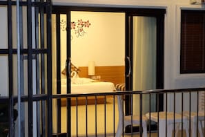 Habitación de hotel con cama, mesita de noche, lámpara y vista al exterior por una puerta corrediza.