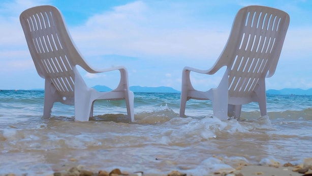 Deux chaises en plastique blanches sur une plage, avec la mer et les montagnes en arrière-plan.