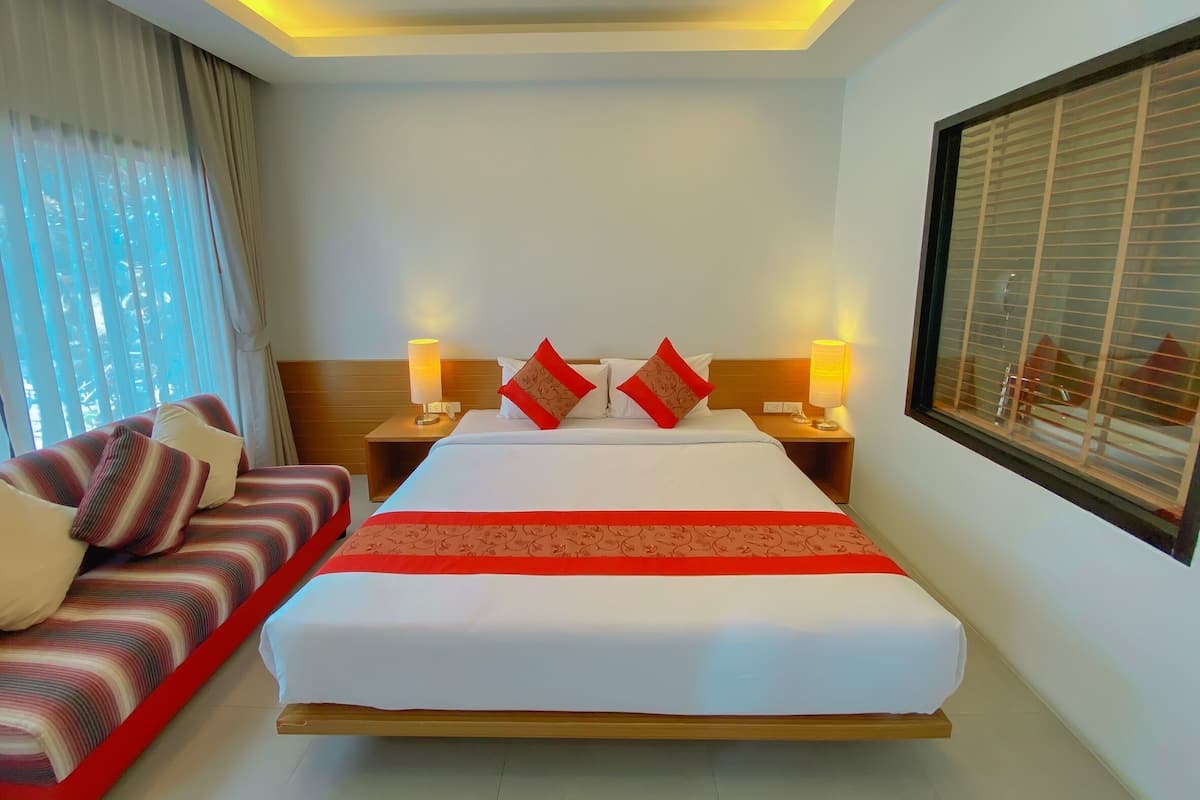 Een hotelkamer met een groot bed, twee nachtkastjes met lampen, een bank met gestreepte kussens en een raam met blinds.
