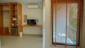 Une chambre moderne avec un bureau en bois, une télévision et une grande fenêtre équipée de stores.