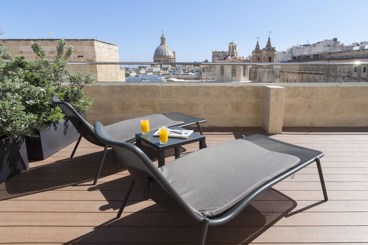 Une terrasse sur le toit avec un fauteuil de relaxation, une table avec une boisson et une plante en pot.