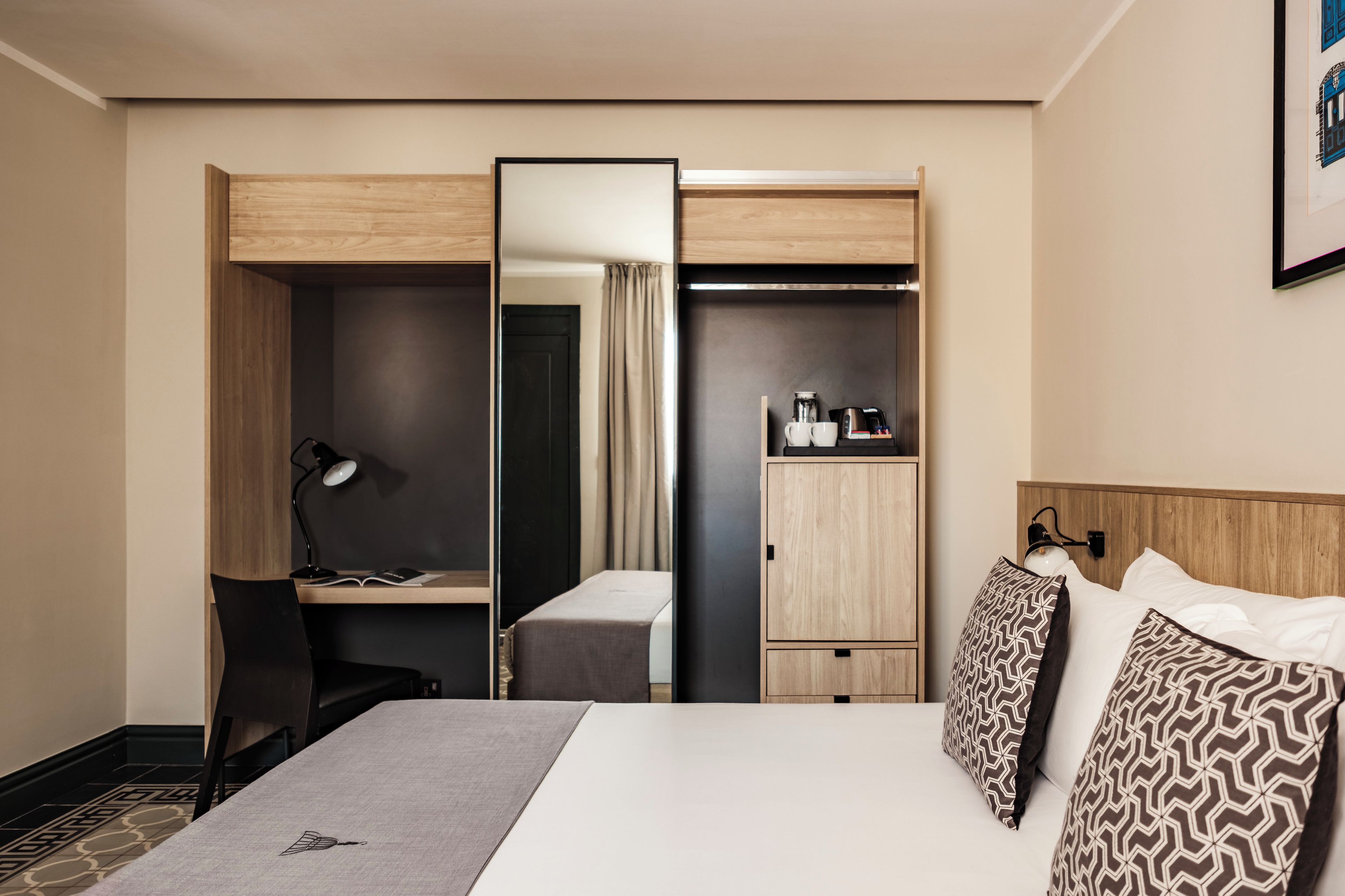 A hotel room with a bed, desk, chair, and wardrobe.