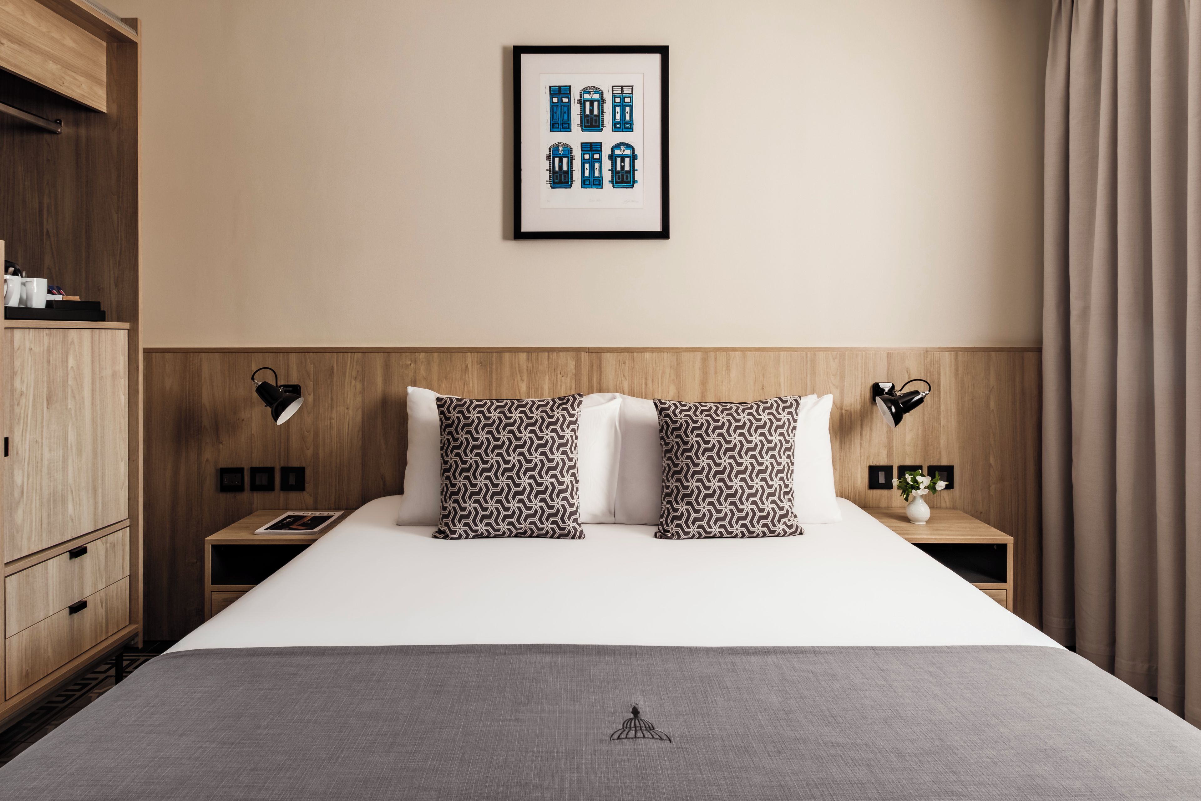 A hotel room with a bed, two nightstands, a wardrobe, a framed picture on the wall, and a curtain.