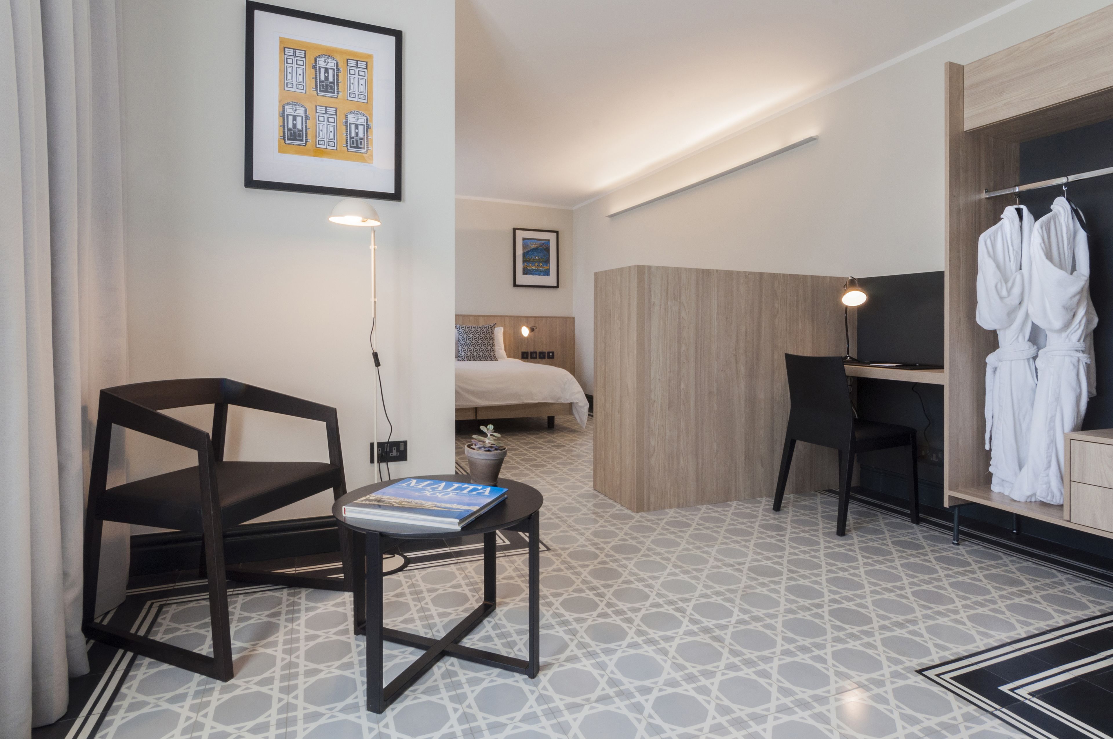 Habitación de hotel pequeña con cama, escritorio, silla y una mesita con un libro.
