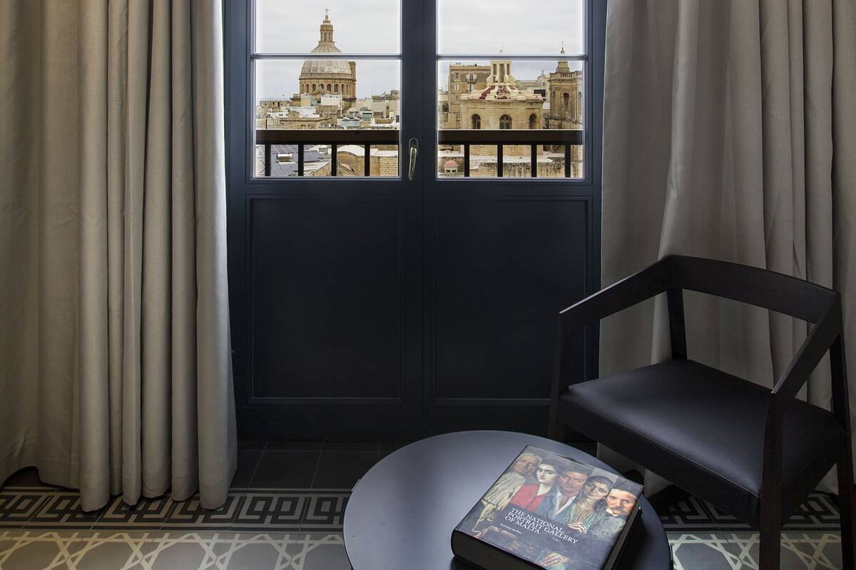Une pièce avec une grande fenêtre, une table ronde sur laquelle repose un livre, et une chaise.
