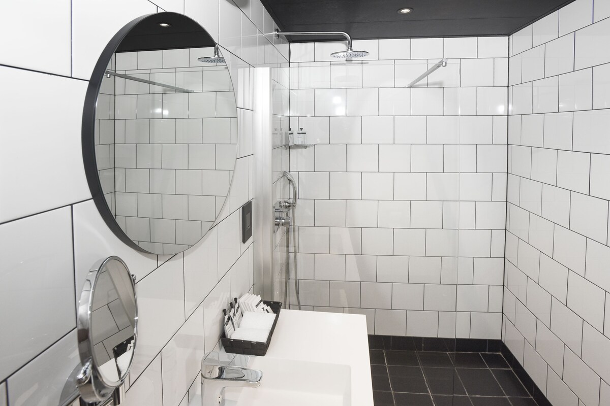 Une salle de bain moderne avec une douche carrelée de carreaux blancs, un miroir rond et un lavabo blanc.