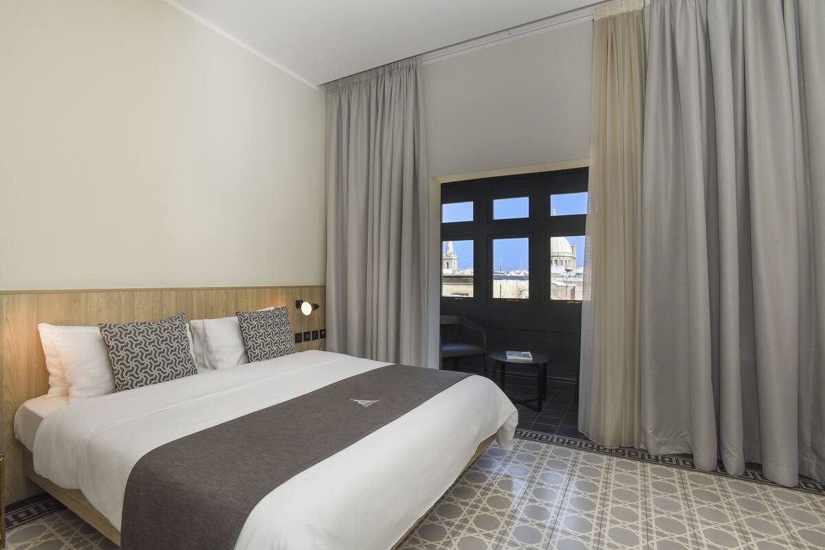 Une chambre d’hôtel avec un grand lit, un bureau et une vue sur un immeuble par la fenêtre.