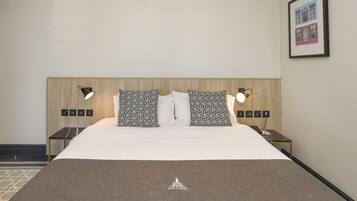 A hotel room with a large bed, two bedside tables, two wall-mounted lamps, and a framed picture on the wall.