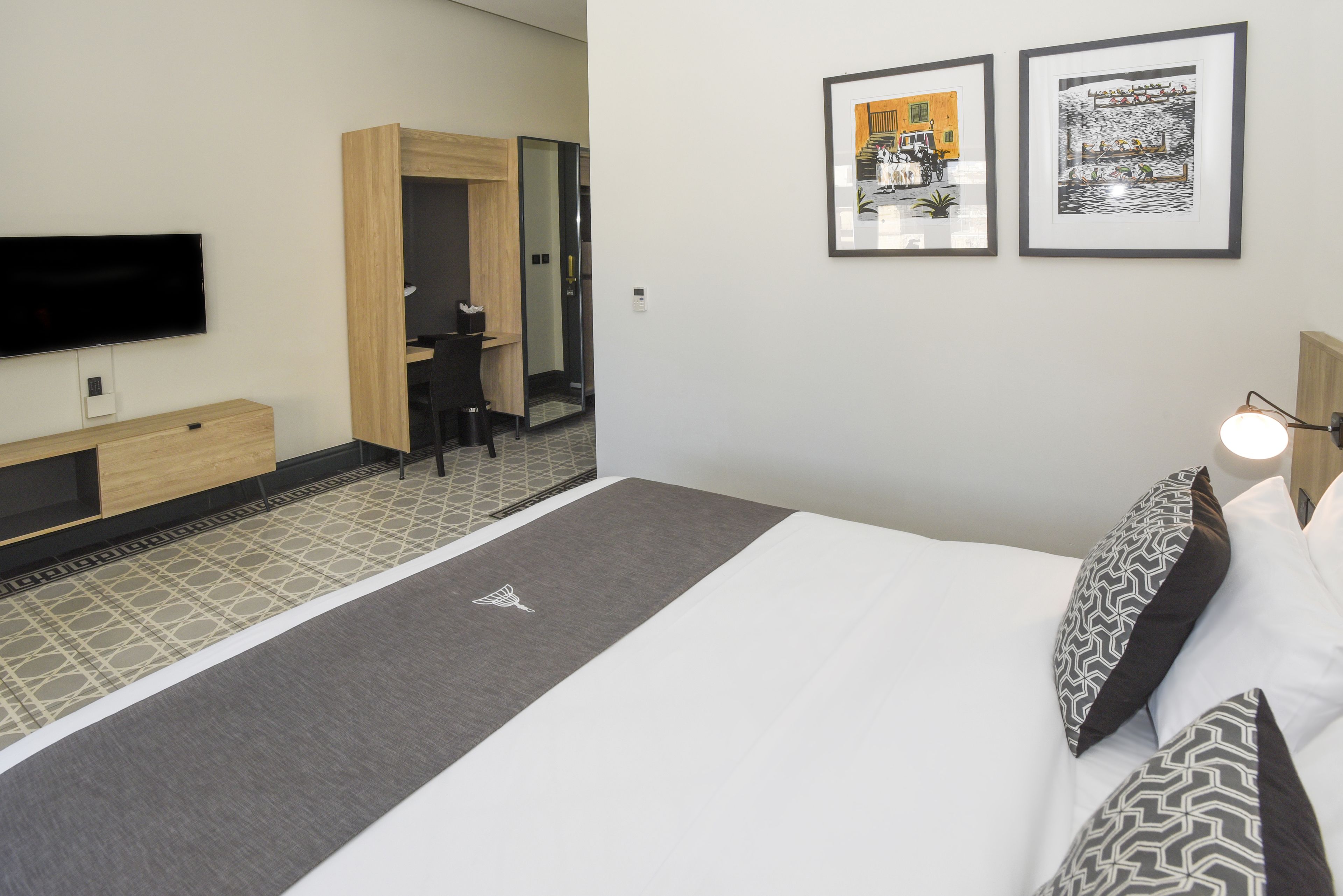 Une chambre d’hôtel moderne équipée d’un téléviseur à écran plat, d’un lit agrémenté d’oreillers à motifs, d’une table de chevet et d’un petit bureau.