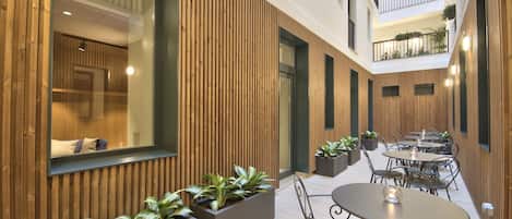 A modern indoor courtyard with wooden paneling, outdoor seating, and potted plants.
