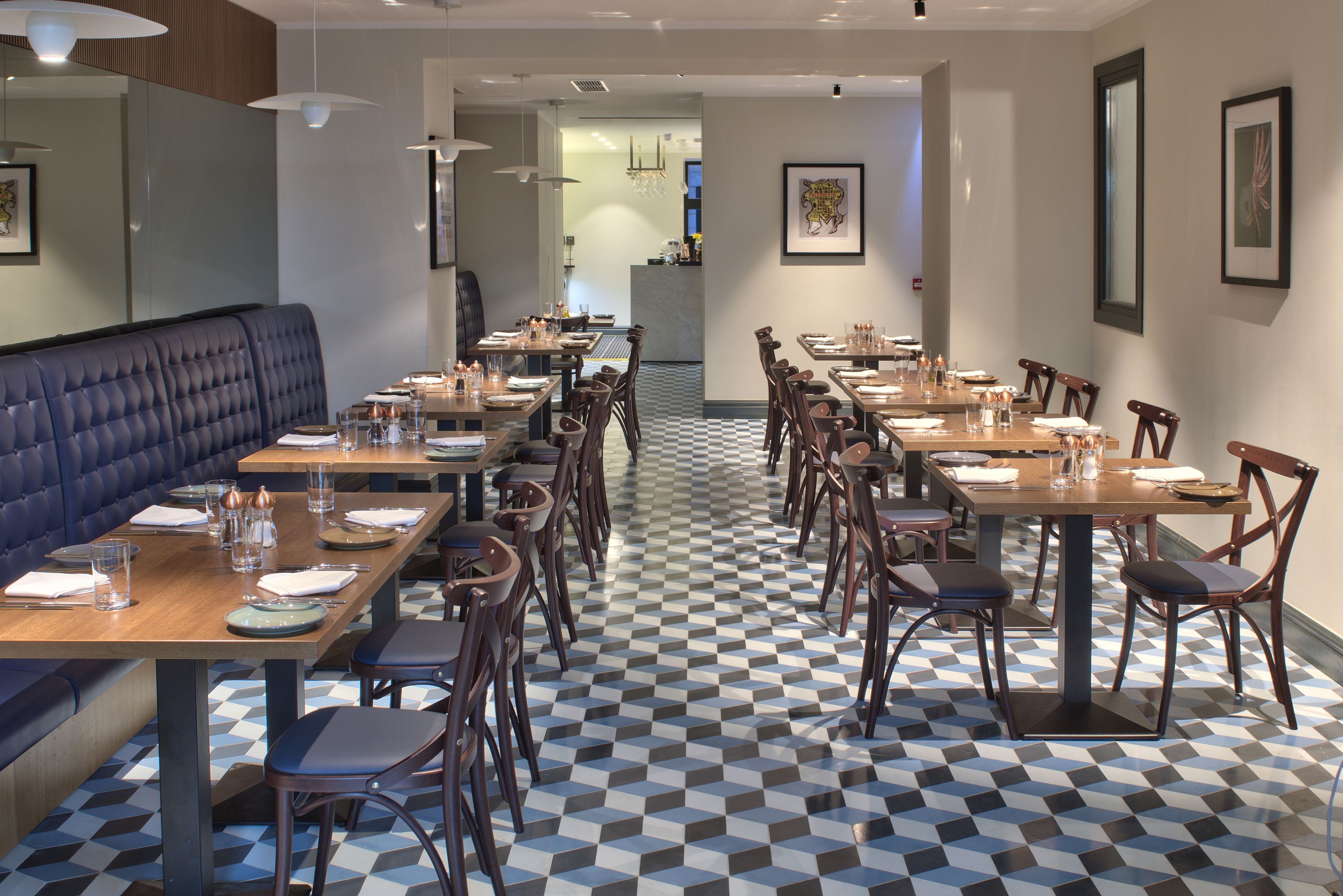 A restaurant with a checkered floor, wooden tables, and chairs. There is a blue booth seating area and a bar in the background.