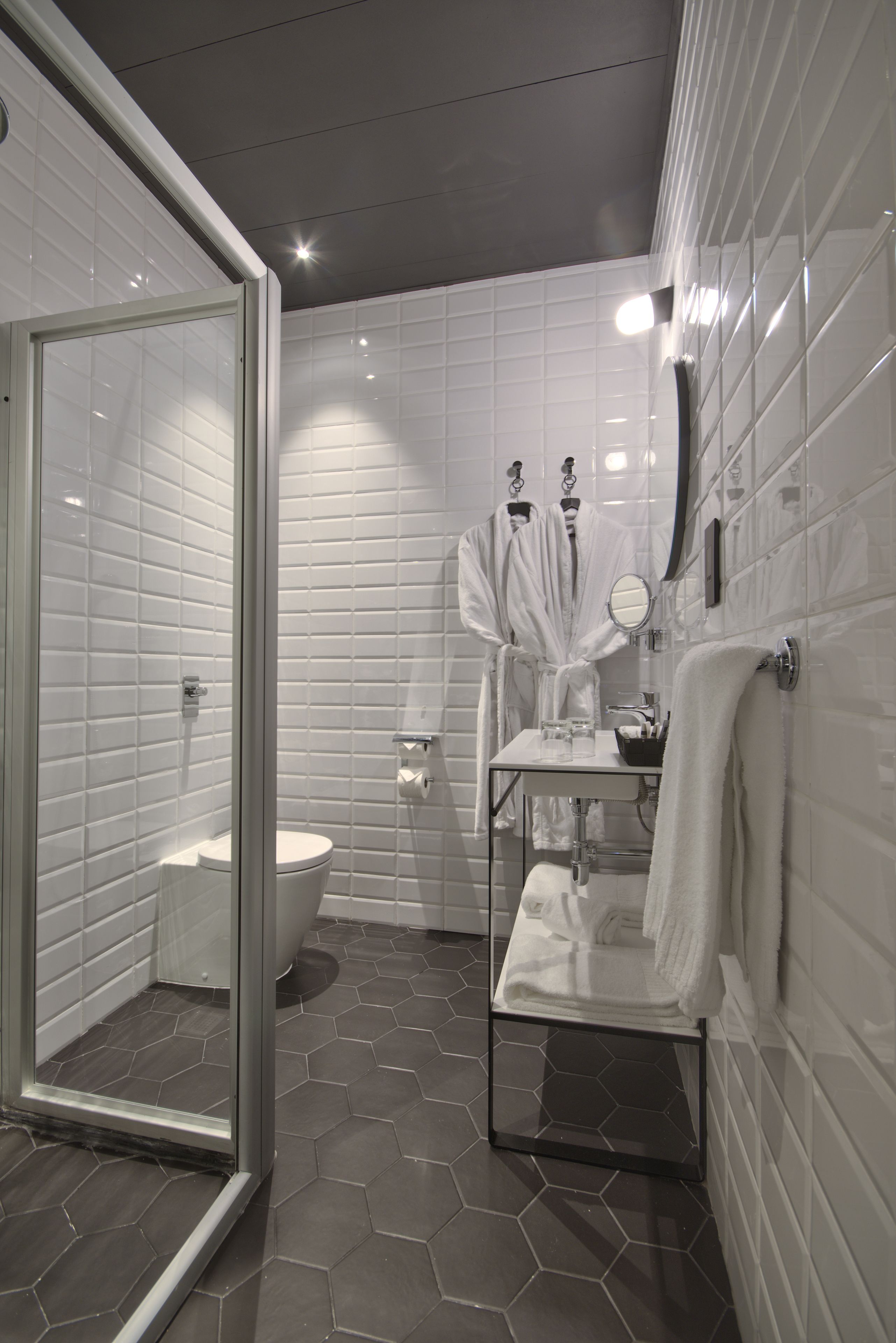 A modern bathroom with white tiles, a glass shower enclosure, a toilet, and a sink with a mirror.