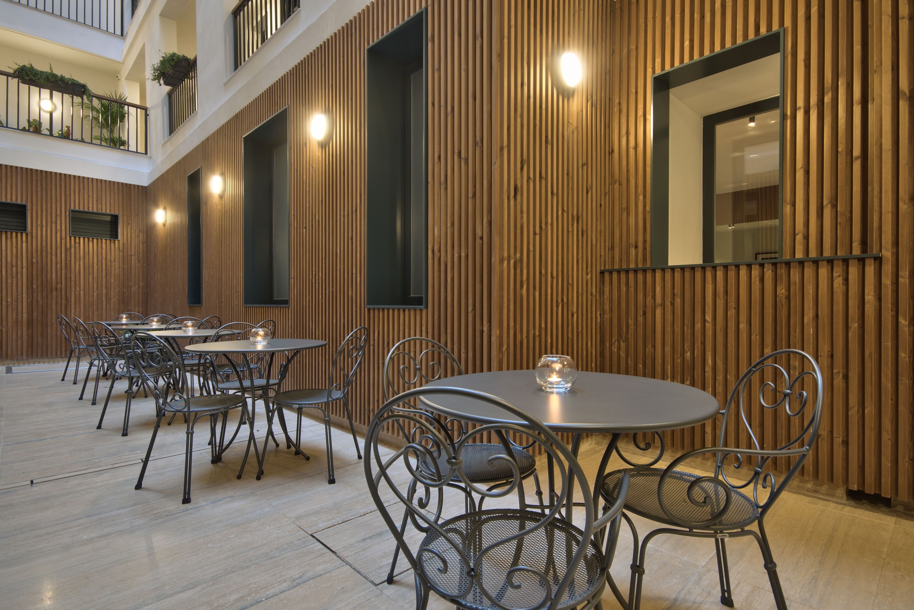 Un vaste espace de restauration intérieur, doté de plusieurs tables rondes et de chaises en métal, de murs recouverts de panneaux de bois et d’un haut plafond avec un balcon.