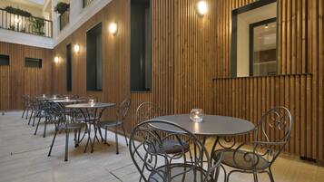 Un vaste espace de restauration intérieur, doté de plusieurs tables rondes et de chaises en métal, de murs recouverts de panneaux de bois et d’un haut plafond avec un balcon.