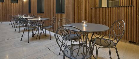 A spacious indoor dining area with multiple round tables and metal chairs, wooden panel walls, and a high ceiling with a balcony.
