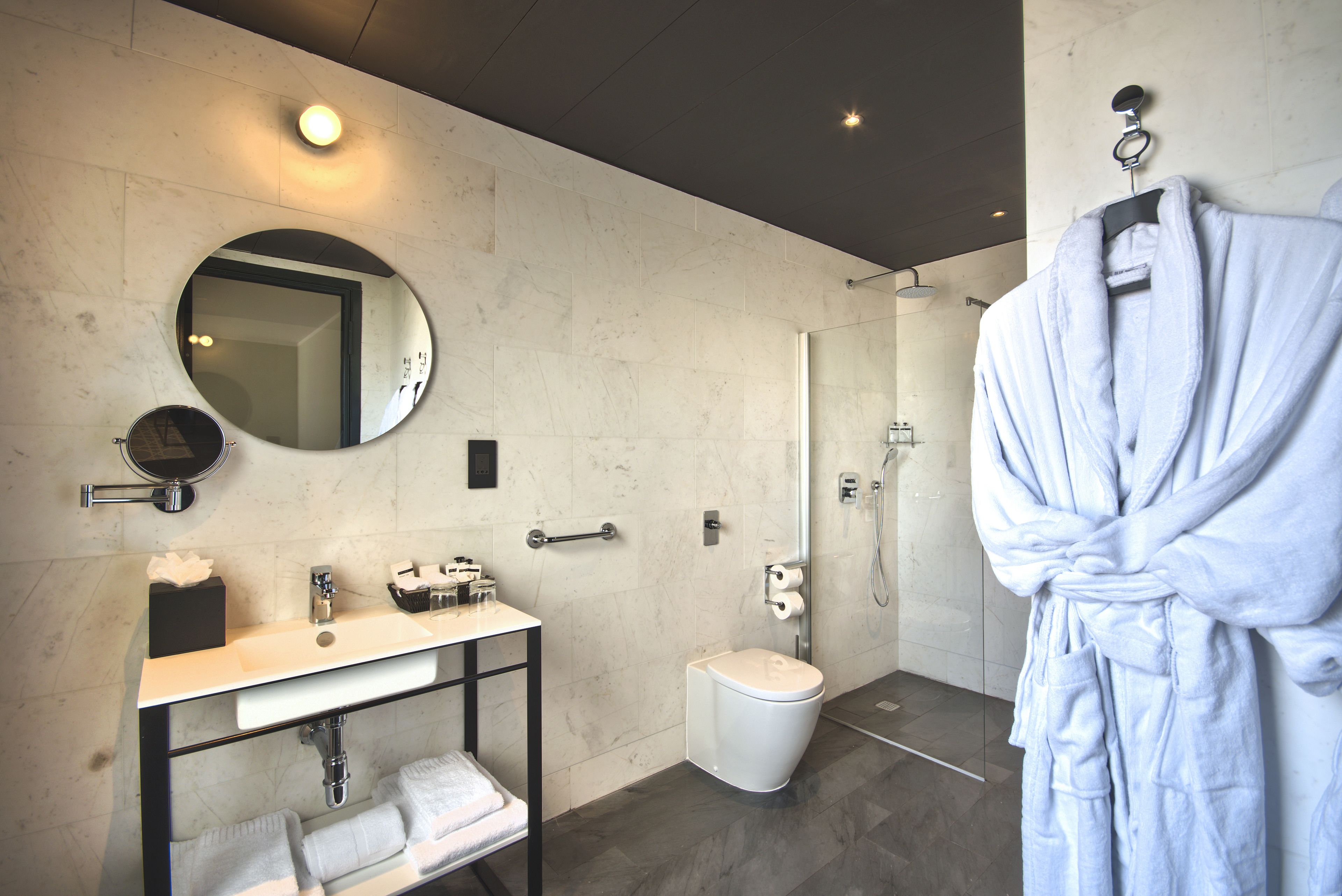 A modern bathroom with a round mirror, a sink, a toilet, and a robe hanging on the wall.
