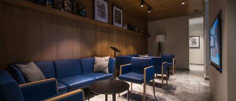 A modern waiting area with blue seating, a wooden wall with framed pictures, and a marble floor.
