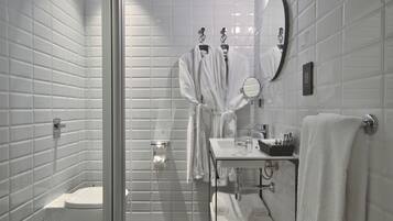 Ein modernes Badezimmer mit weißen Fliesen, einer Duschkabine aus Glas, einem weißen Waschbecken mit Spiegel und einem Handtuchhalter.