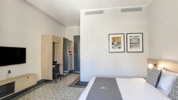 A modern hotel room with a large bed, a flat-screen TV, a desk, and two framed pictures on the wall.