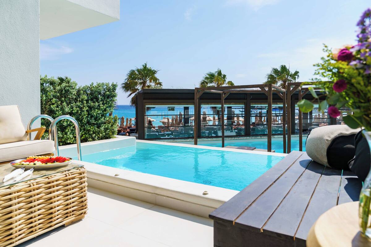 Zona de piscina con vista al océano, sillas de descanso y una mesa de comedor con una cesta de fruta.