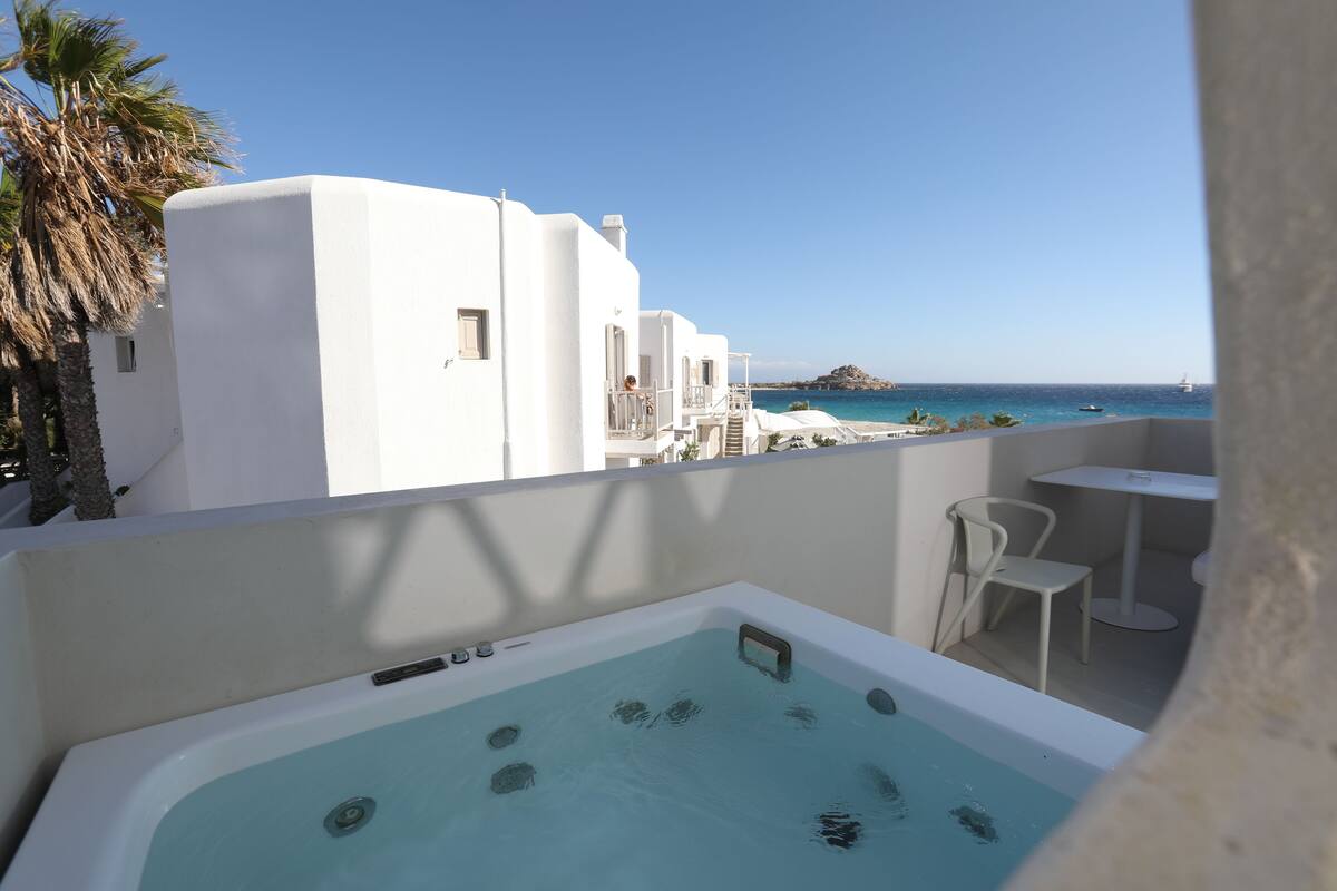 Un balcón con hidromasaje, edificios blancos, una palmera y vistas al mar.