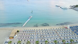 A beach with a pier, lounge chairs, umbrellas, and boats. - Mykonos Dove Beachfront Hotel (Mykonos)