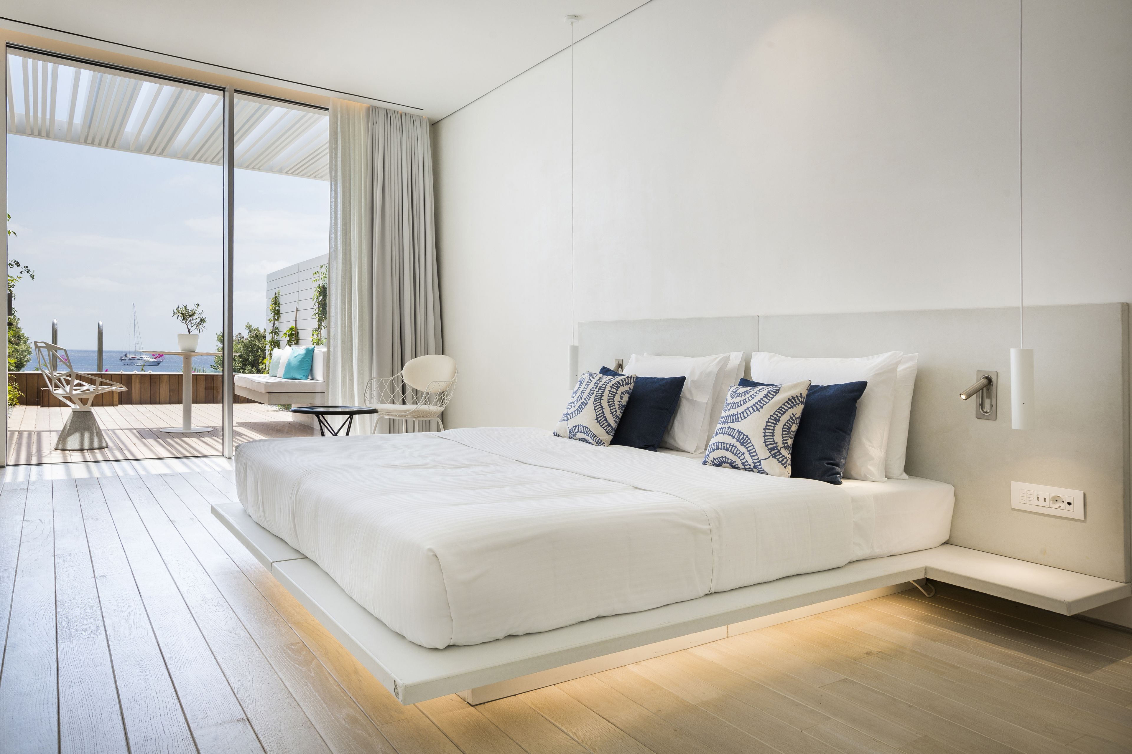 A modern bedroom with a large bed, a view of the sea, and a balcony with outdoor furniture.