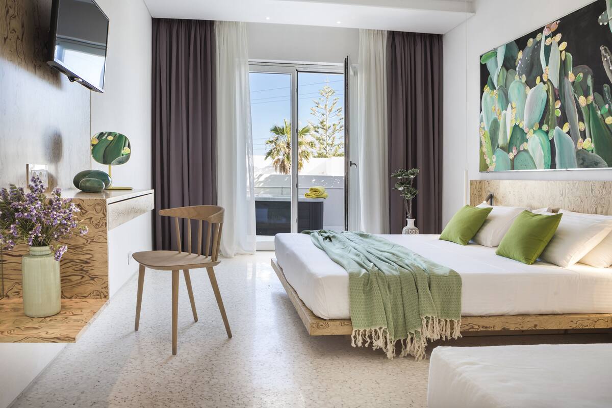 Un dormitorio con cama, una silla, televisor montado en la pared y un cuadro.